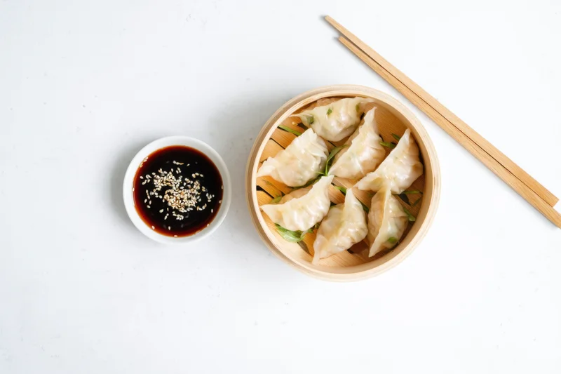 Bamboo steamer with dumplings and soy sauce on white surface