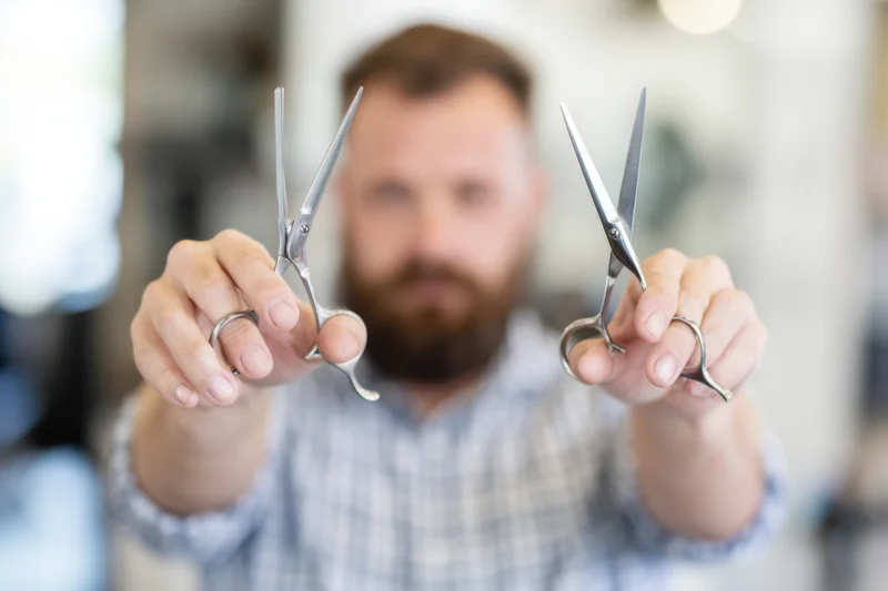 Barber holding two pairs of scissors toward camera in salon setting