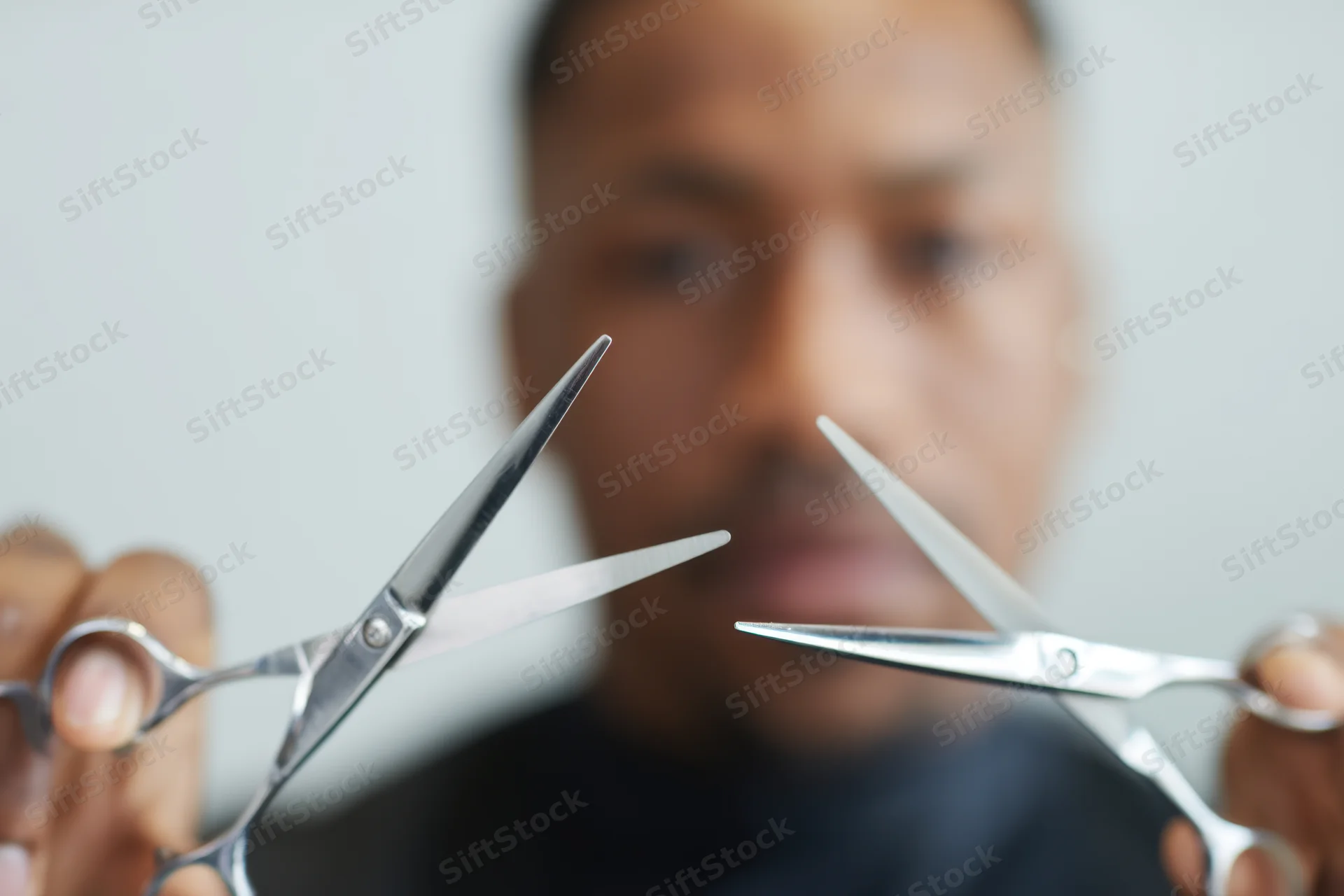 Barber holding two pairs of scissors in focus with blurred face in background