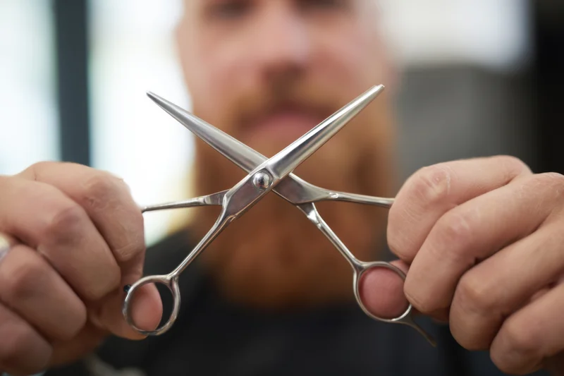 Barber holding crossed scissors in focus with blurred face in background