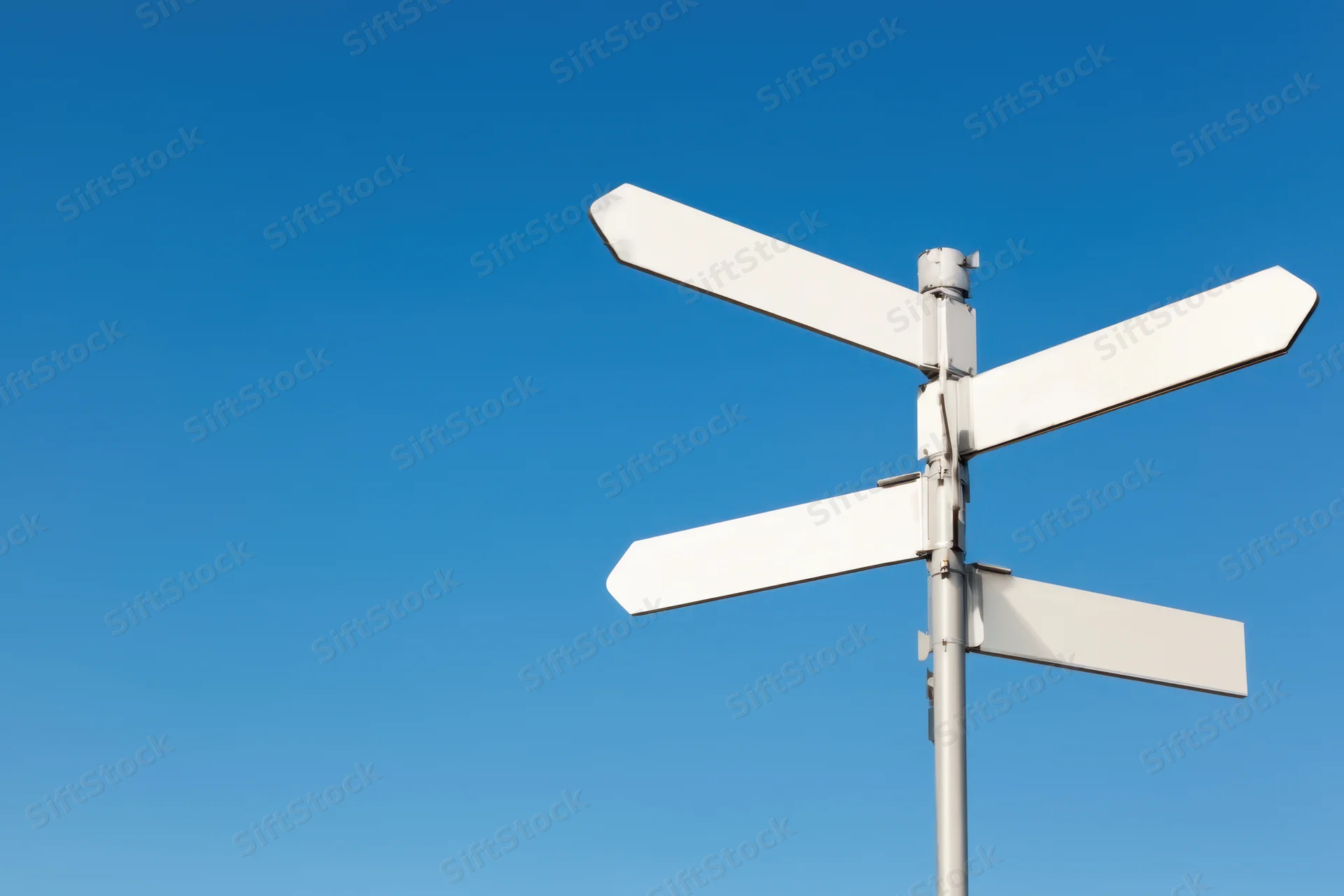 Blank directional signpost with four white arrows against a clear blue sky