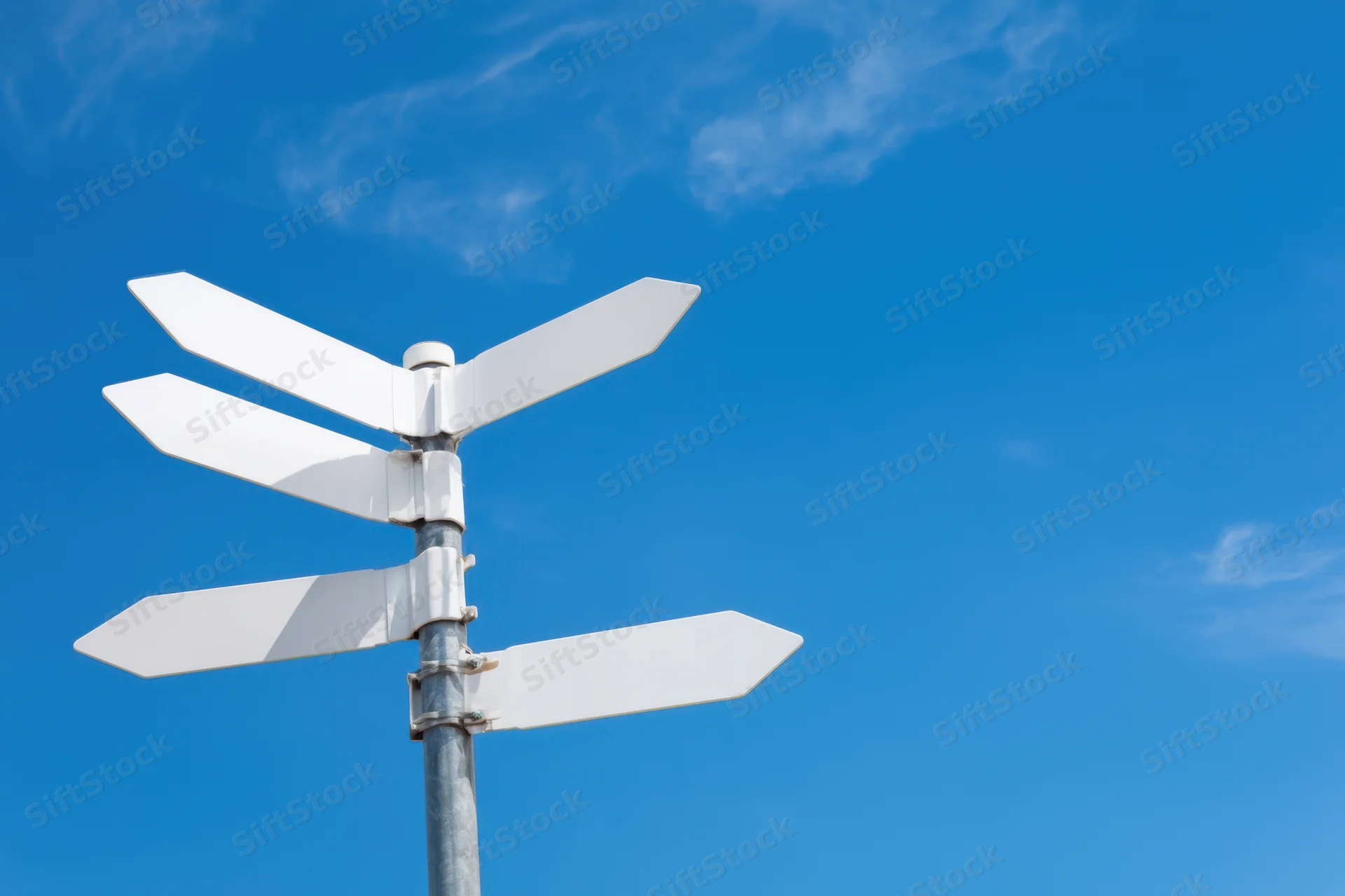 Blank white directional signpost with multiple arrows against a clear blue sky