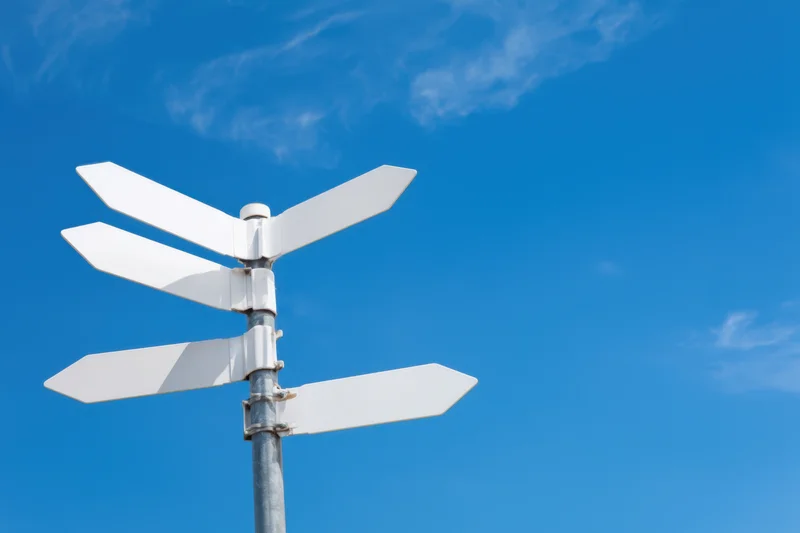 Blank white directional signpost with multiple arrows against a clear blue sky