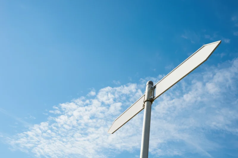 Blank white directional sign on metal pole against blue sky with scattered clouds