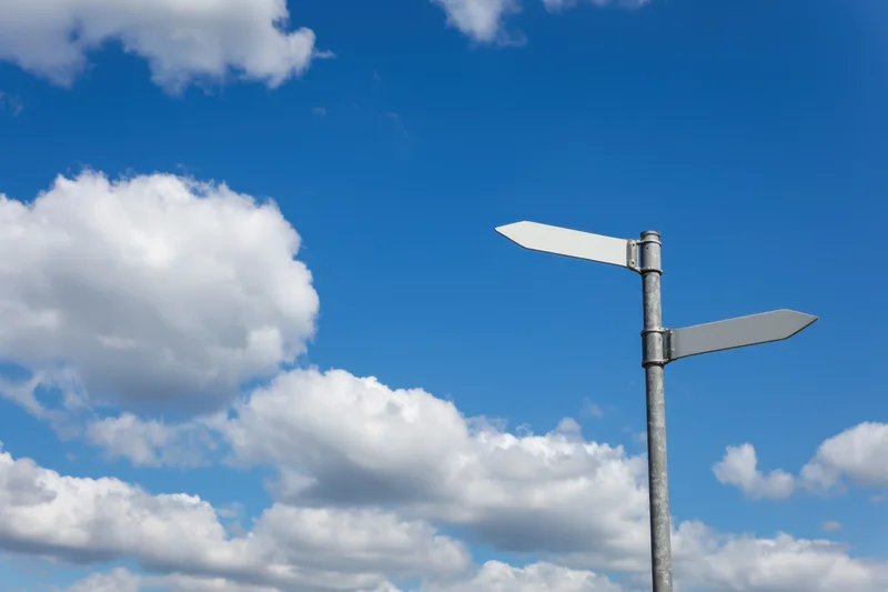 Blank metal sign with two directional arms pointing against a blue sky with white clouds