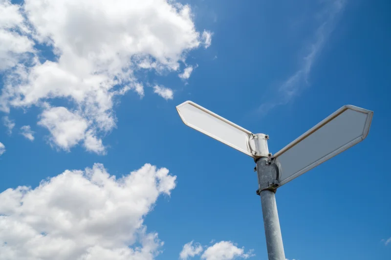 Blank street sign pointing in two directions against a blue sky with clouds