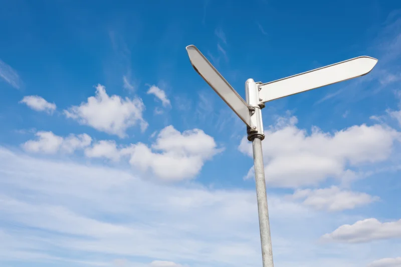 Blank street sign pointing in two directions against a blue sky with scattered clouds
