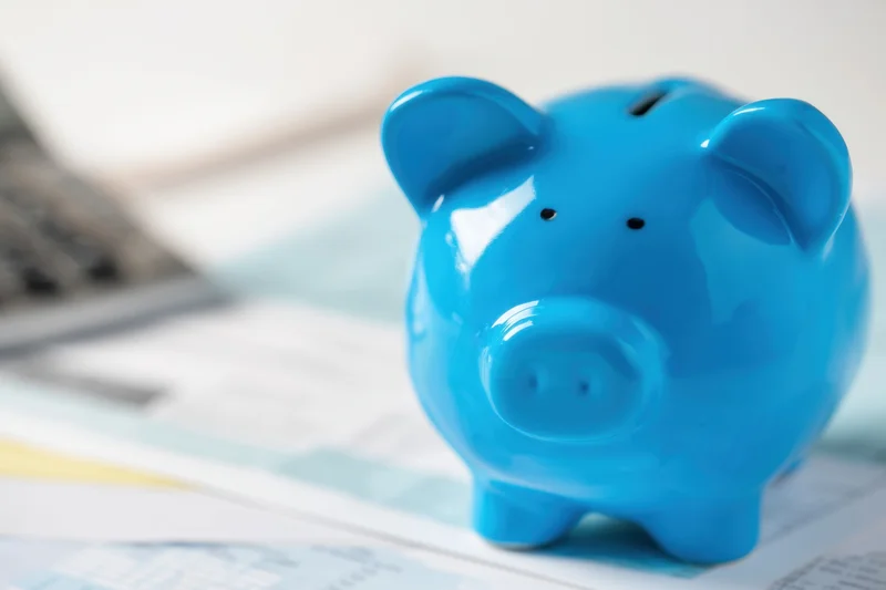 Blue piggy bank sitting on financial documents with calculator nearby on desk
