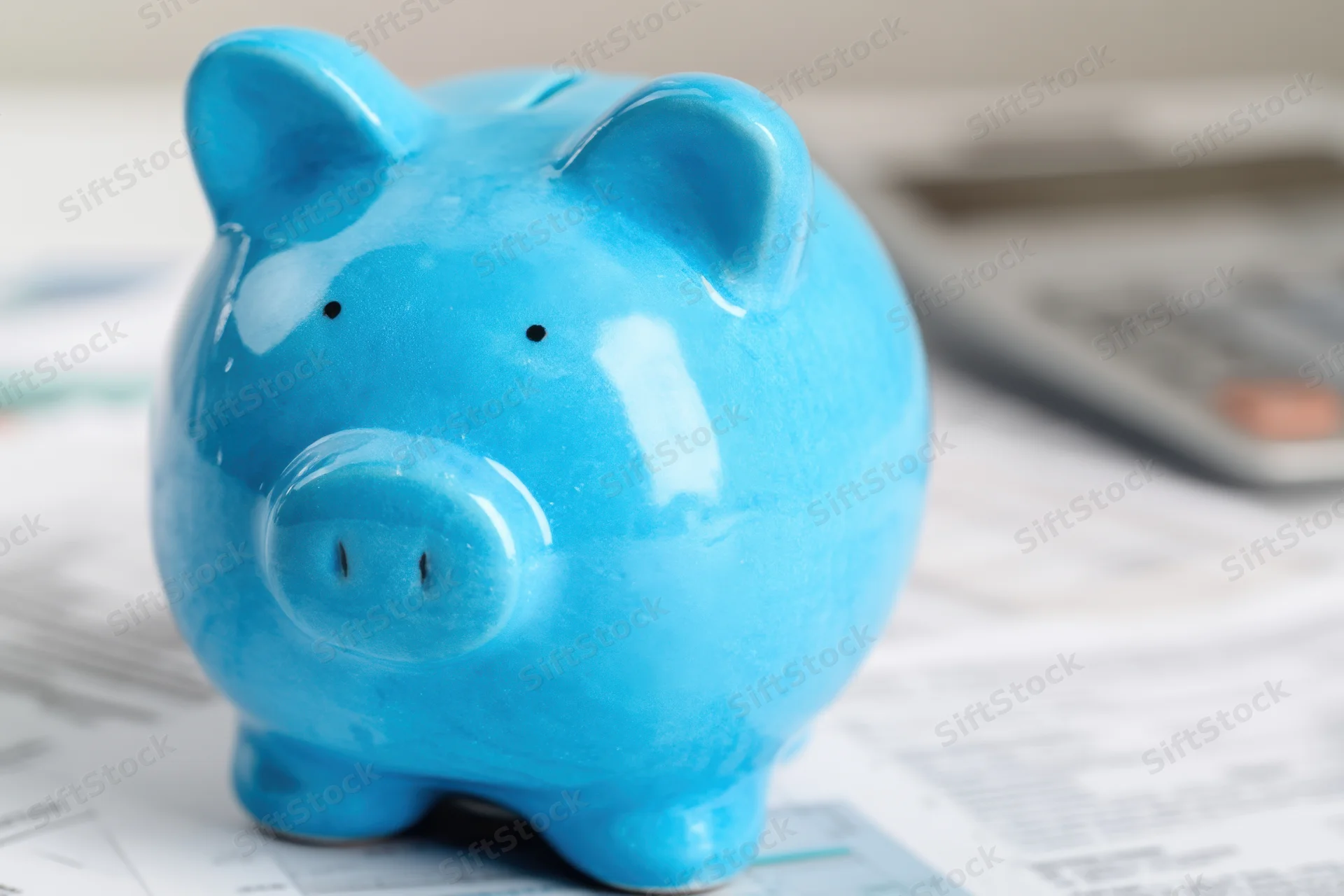 Blue ceramic piggy bank sitting on financial documents with a calculator nearby