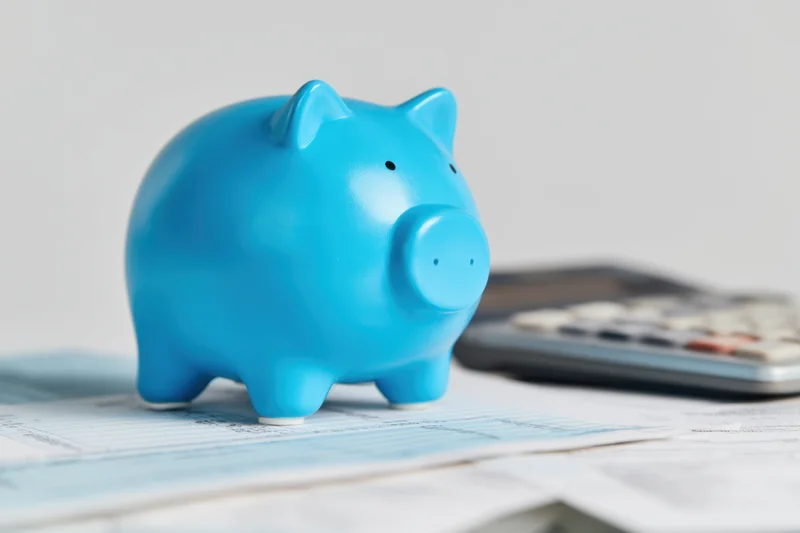 Blue piggy bank on financial documents with calculator nearby