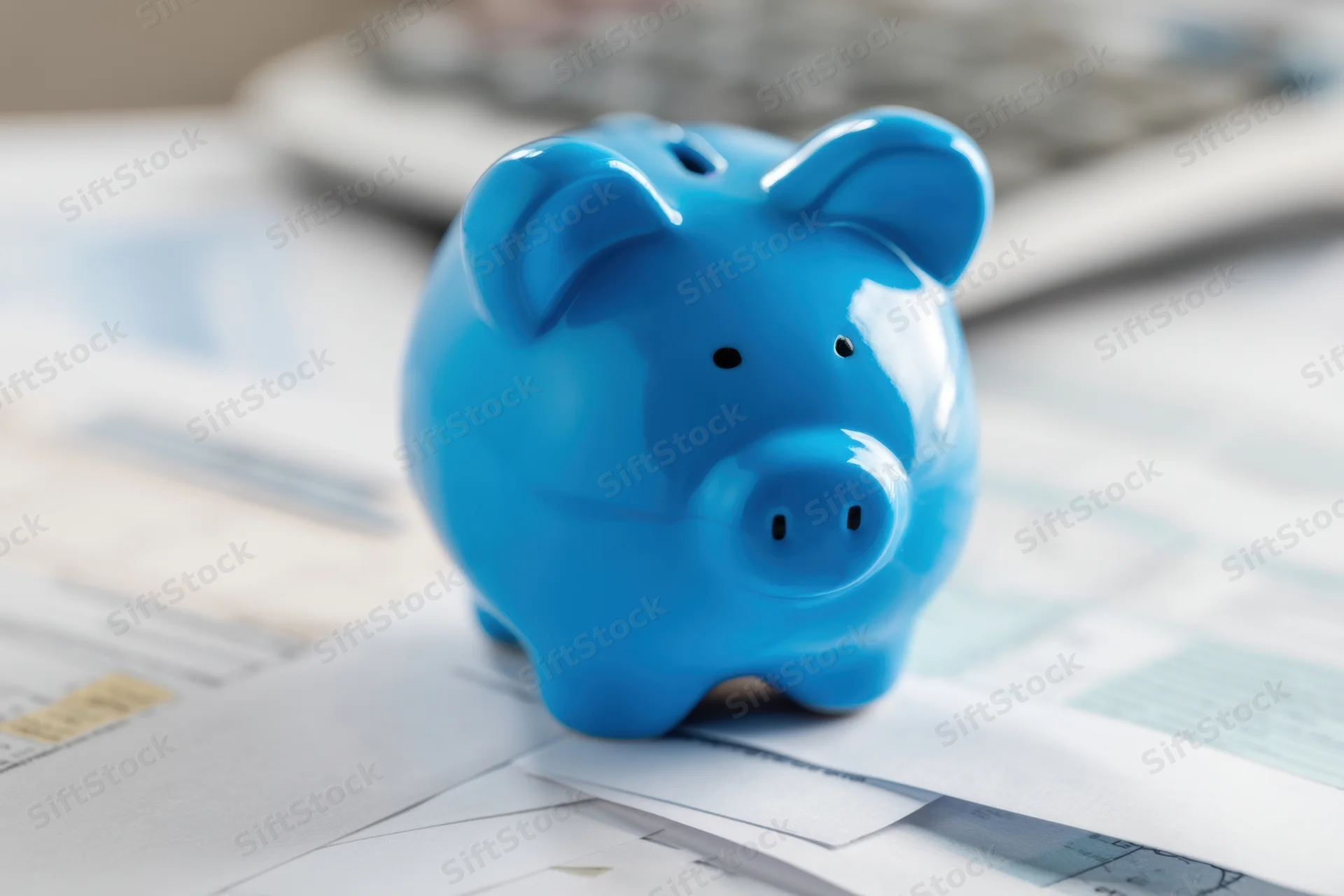 Blue ceramic piggy bank resting on financial documents with calculator in background