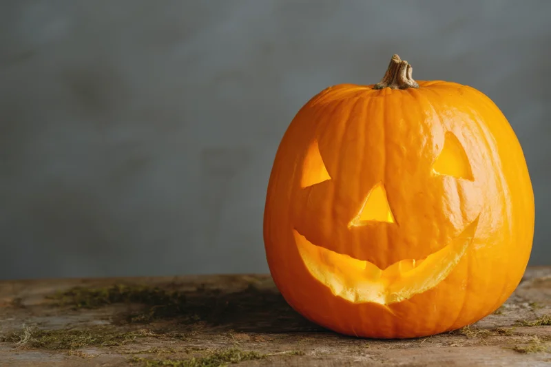 Carved orange pumpkin with smiling face glowing on rustic wooden table with moss accents