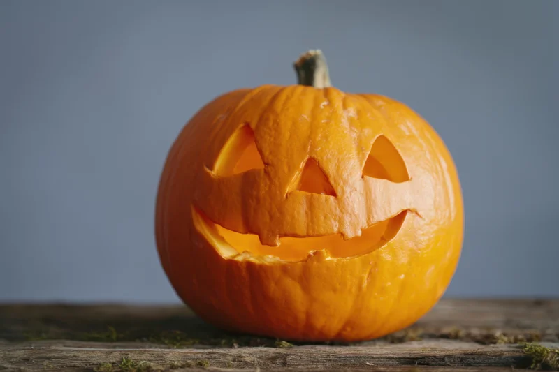 Carved orange pumpkin with smiling face on wooden surface