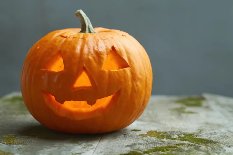 Carved orange pumpkin with smiling face lit from within on a mossy wooden surface