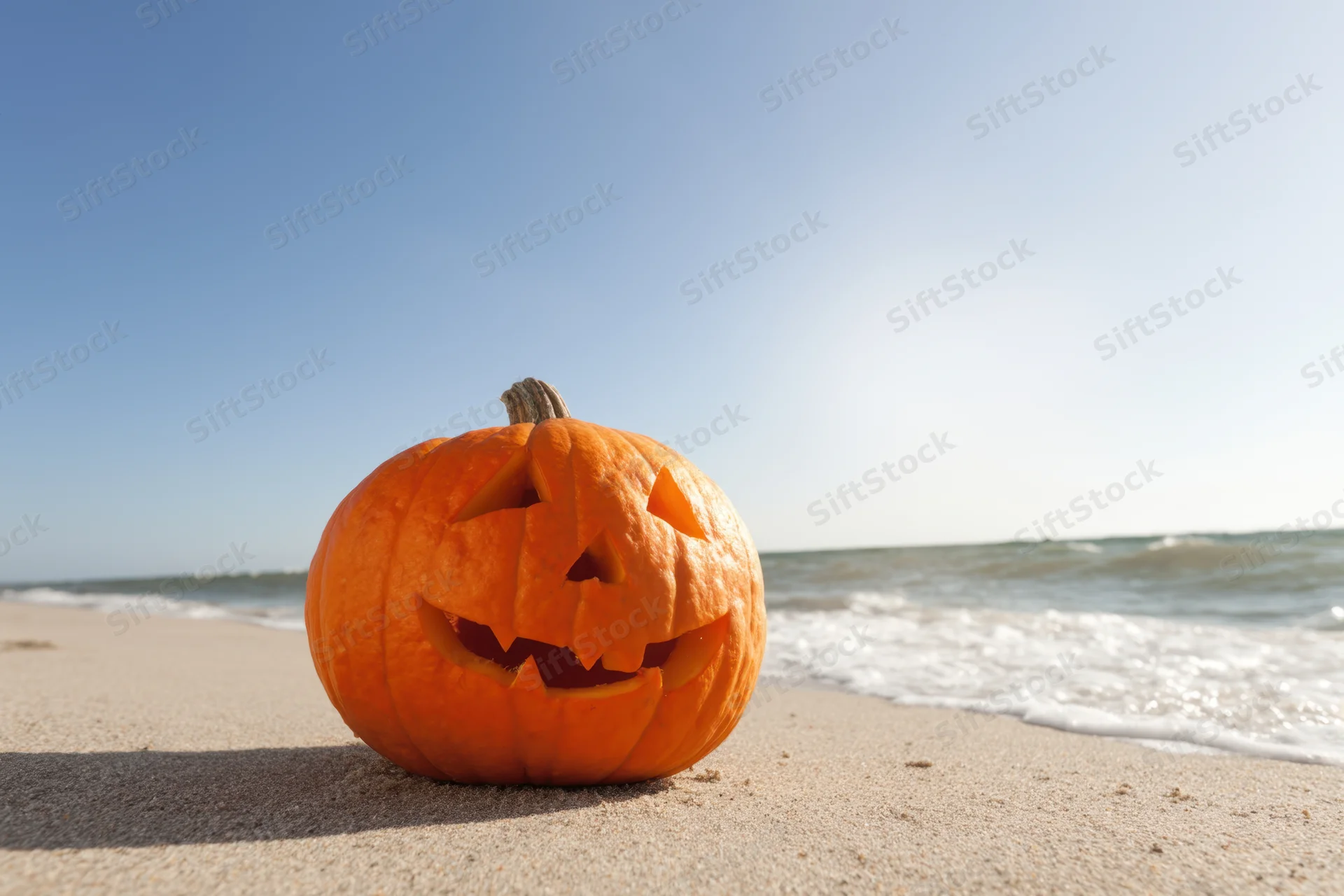 Carved jack-o-lantern sitting on sandy beach near ocean waves
