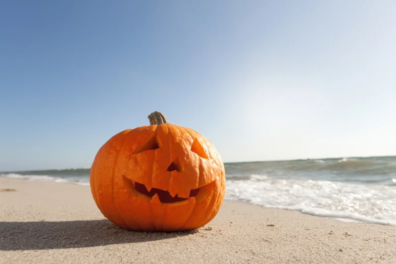 Carved jack-o-lantern sitting on sandy beach near ocean waves
