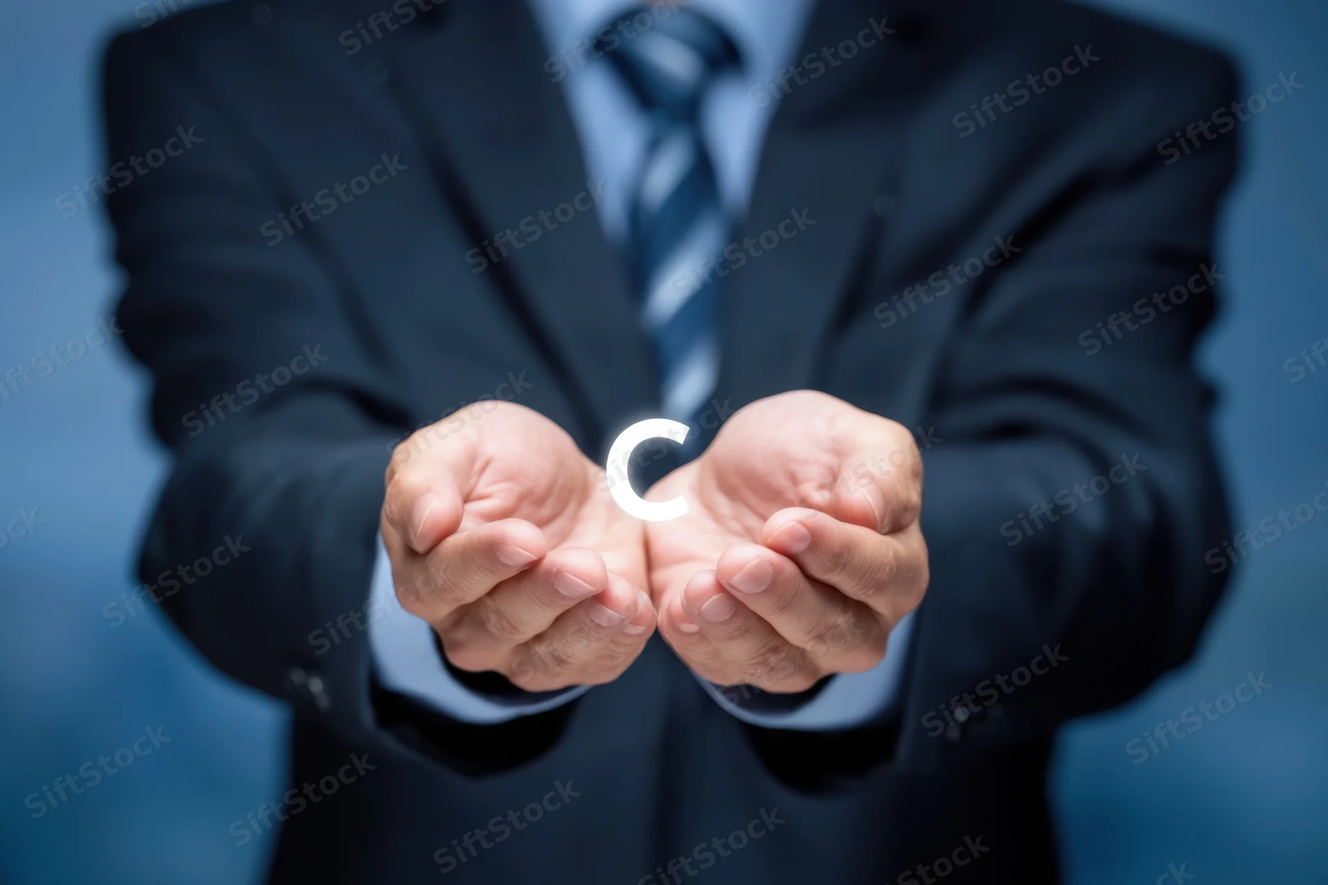 Businessman in suit cradling glowing letter c in hands against blue background