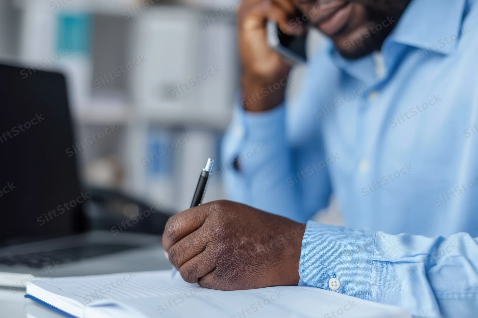 Businessman on phone writing notes at office desk