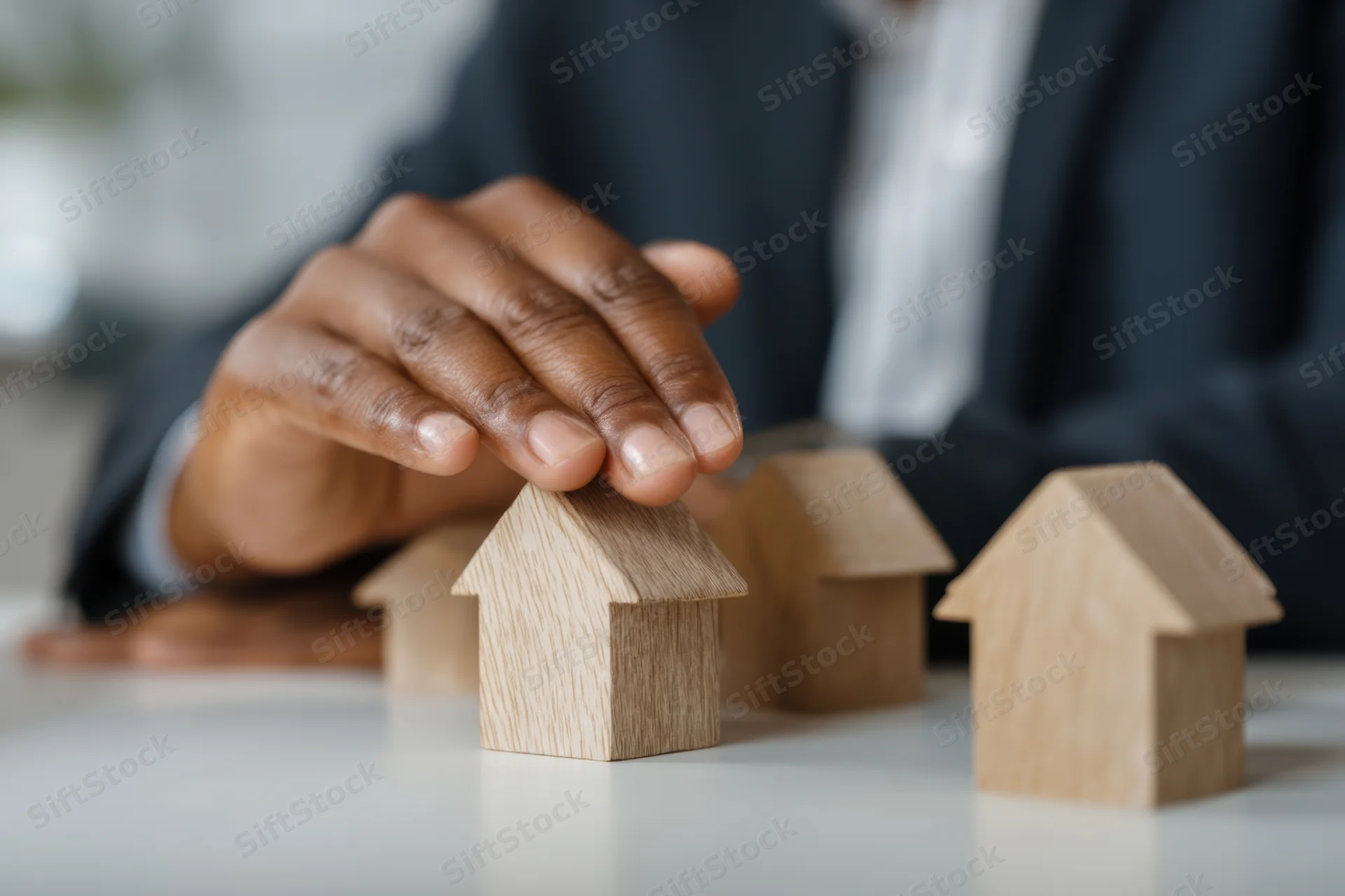 Businessman in suit placing hand on wooden house model on desk
