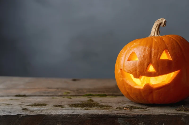 Carved pumpkin with glowing cheerful face on rustic wooden table