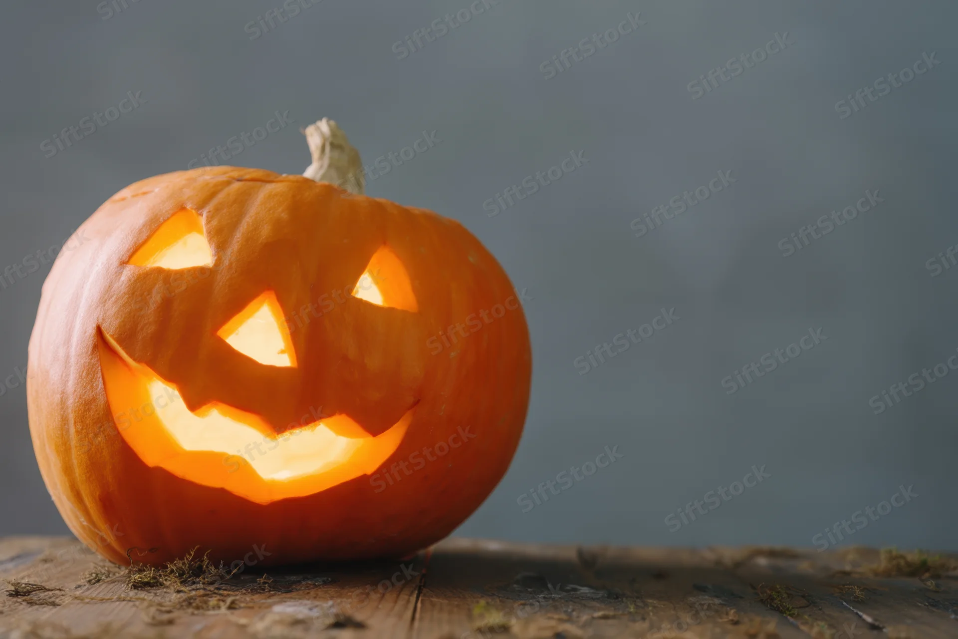 Carved pumpkin with glowing face on wooden surface