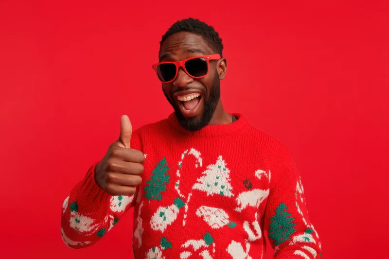 Man in festive red christmas sweater giving thumbs up against red background