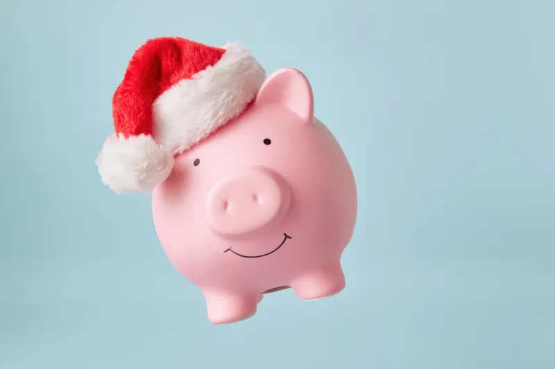 Pink piggy bank wearing santa hat floating against light blue background