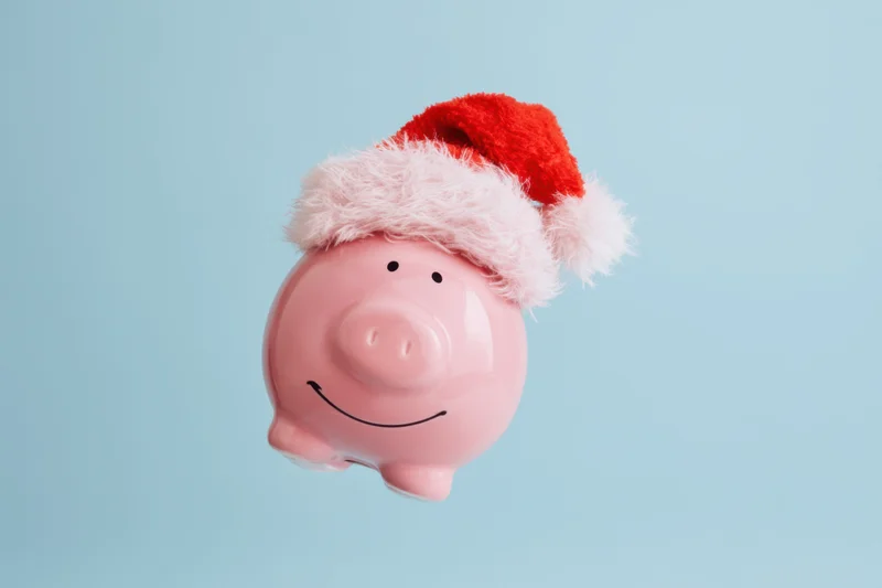 Pink piggy bank wearing santa hat smiling against light blue background