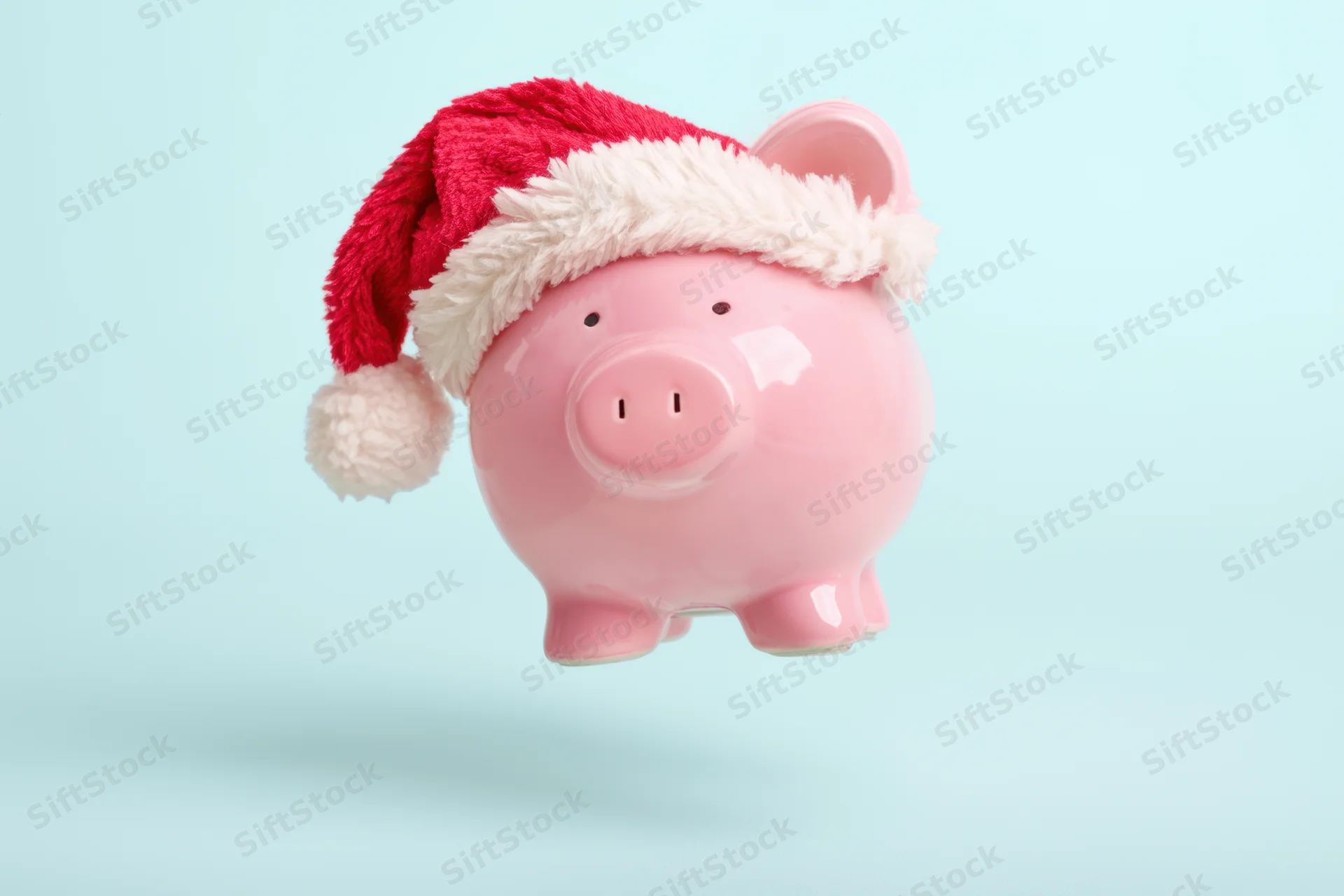 Pink ceramic piggy bank wearing red santa hat floating against light blue background