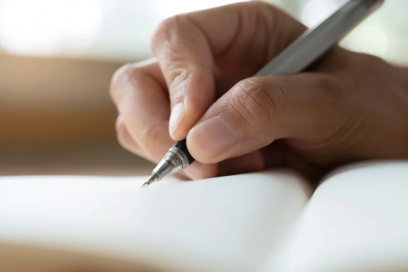Hand holding pen poised to write in open notebook on desk