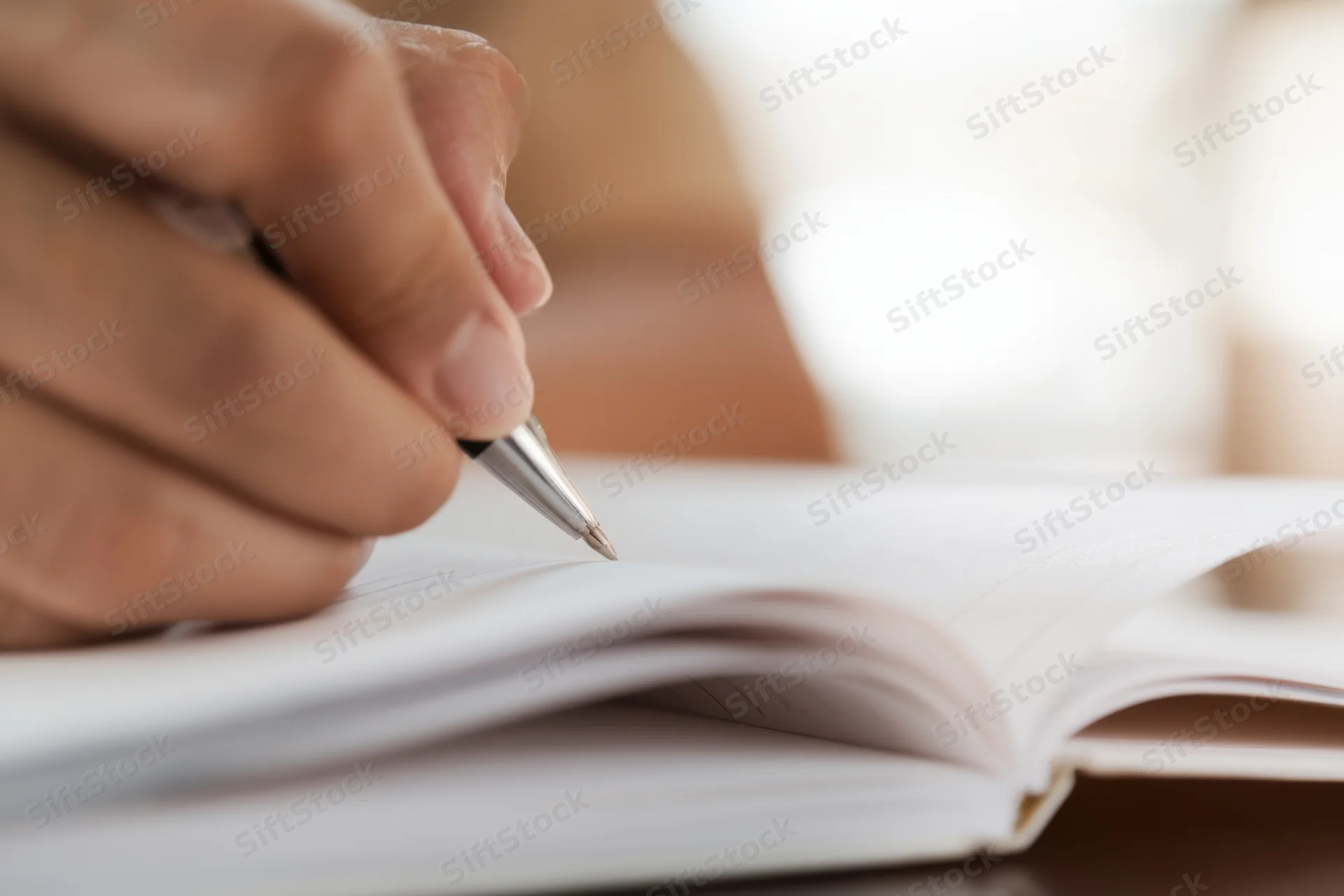 Hand holding pen poised to write in open notebook on desk