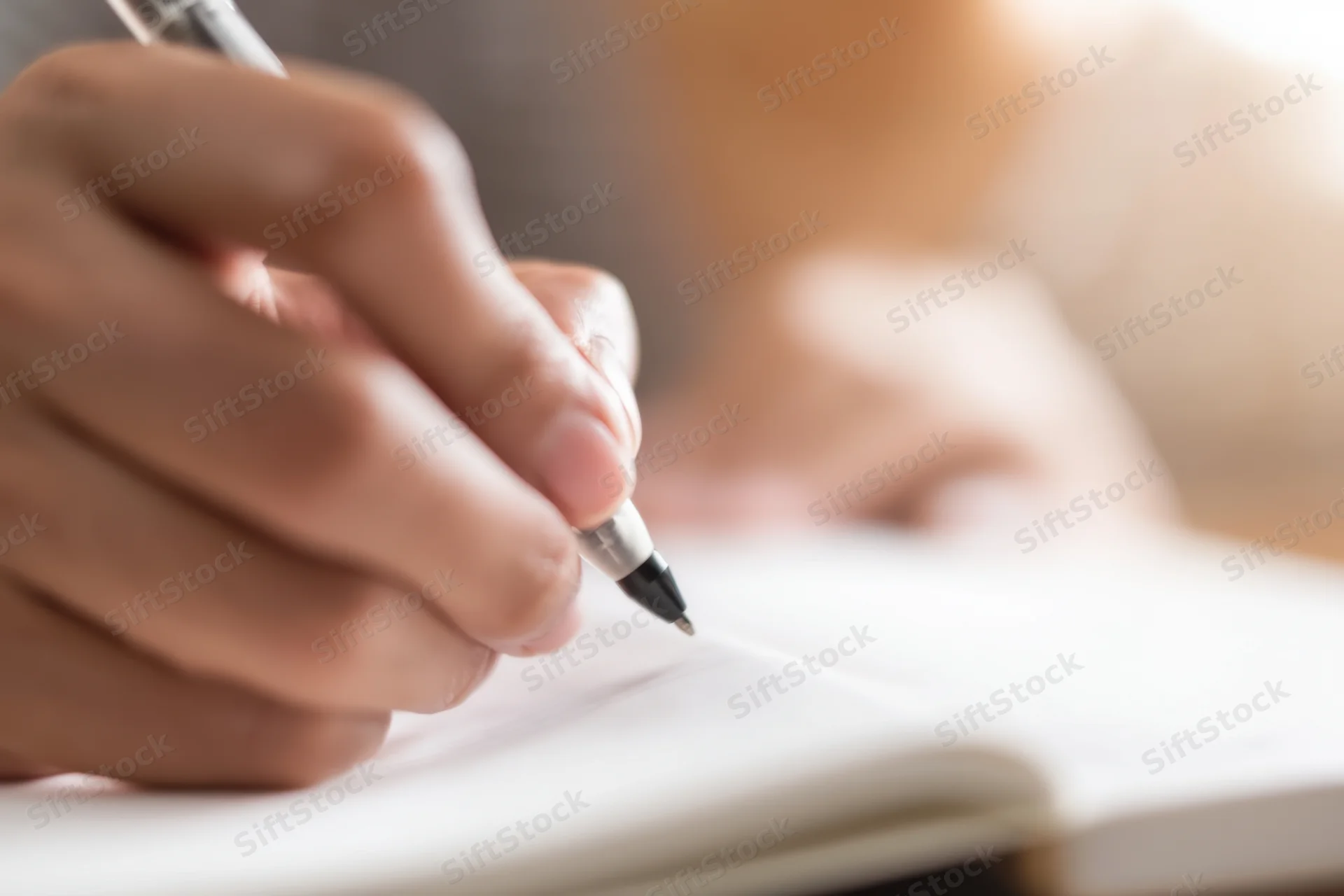 Hand holding pen writing in open notebook on desk
