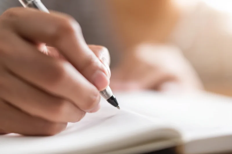 Hand holding pen writing in open notebook on desk
