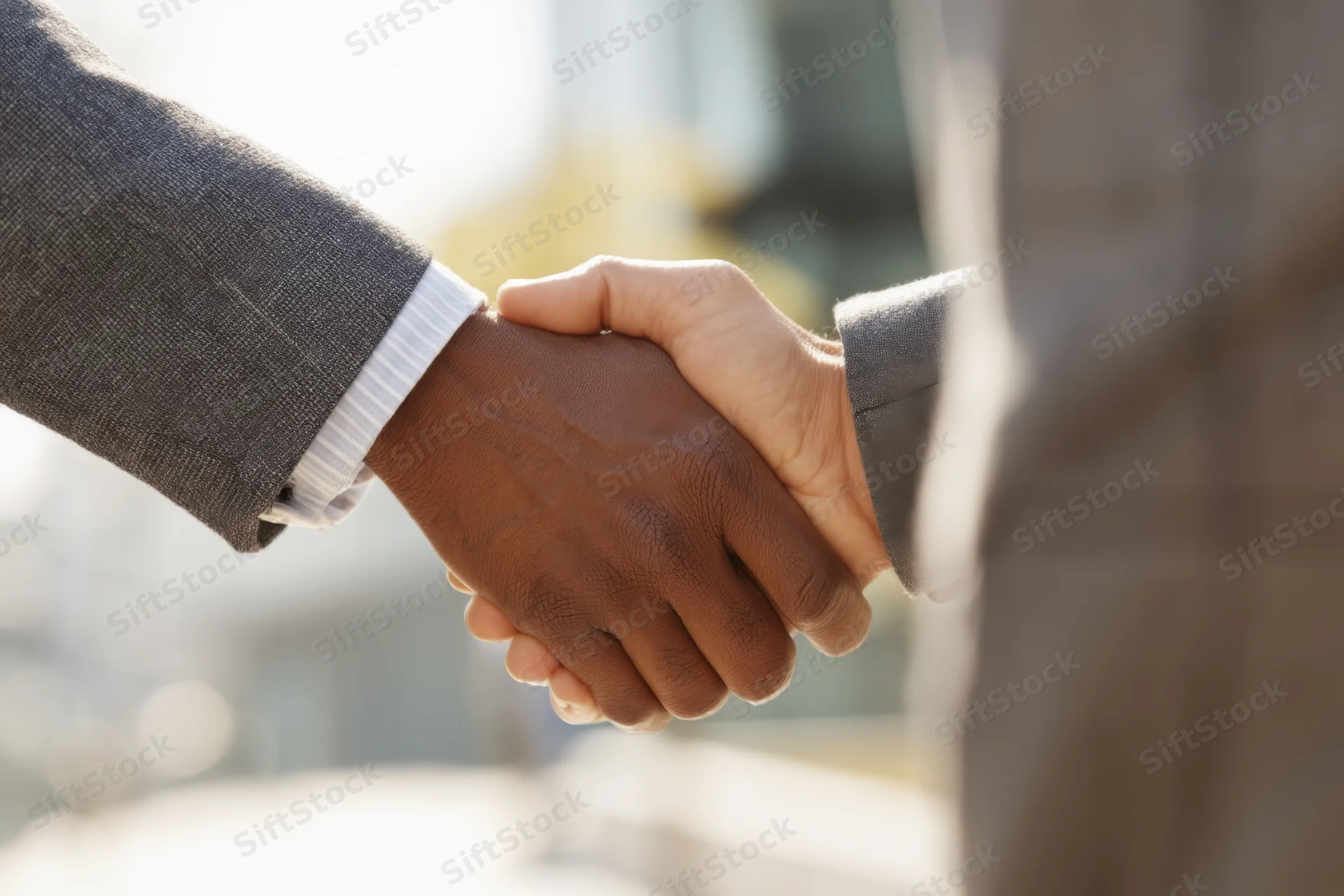 Close-up of two business professionals shaking hands outdoors in formal attire