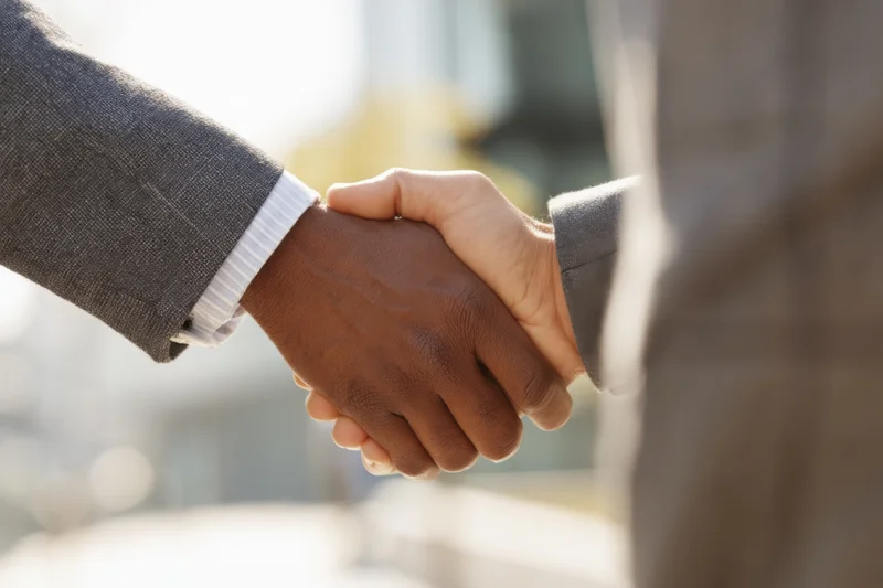Close-up of two business professionals shaking hands outdoors in formal attire