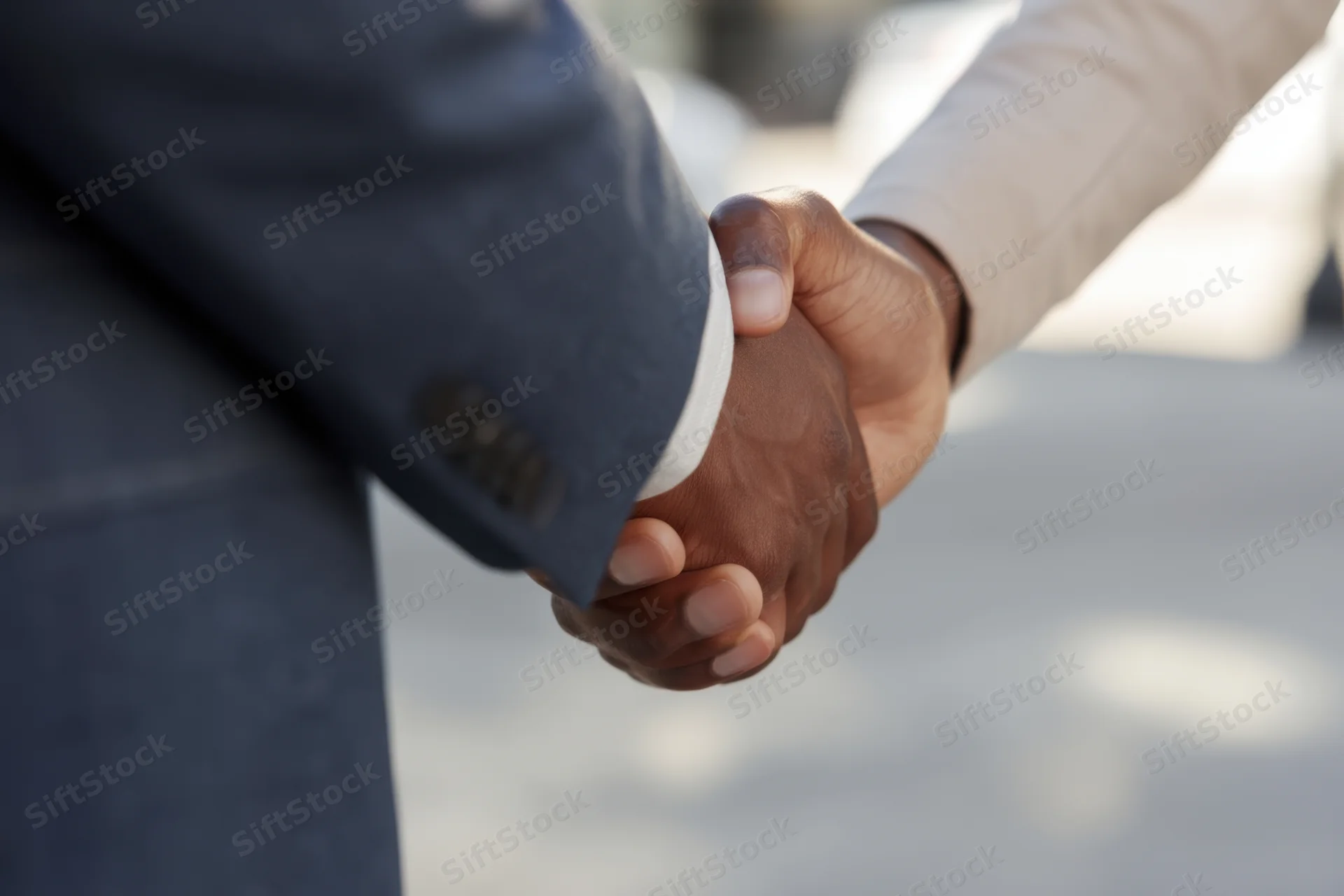Close-up of two business professionals shaking hands in a formal outdoor setting
