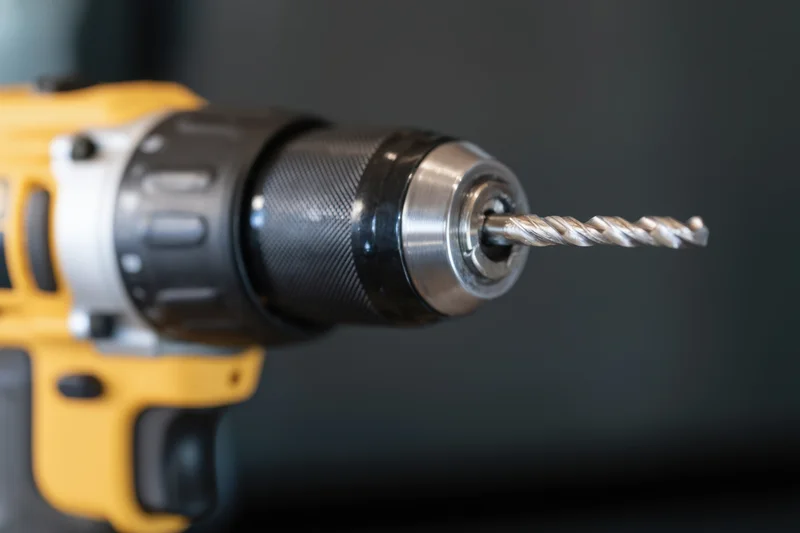 Close-up of a yellow cordless drill with a metallic spiral drill bit in the chuck