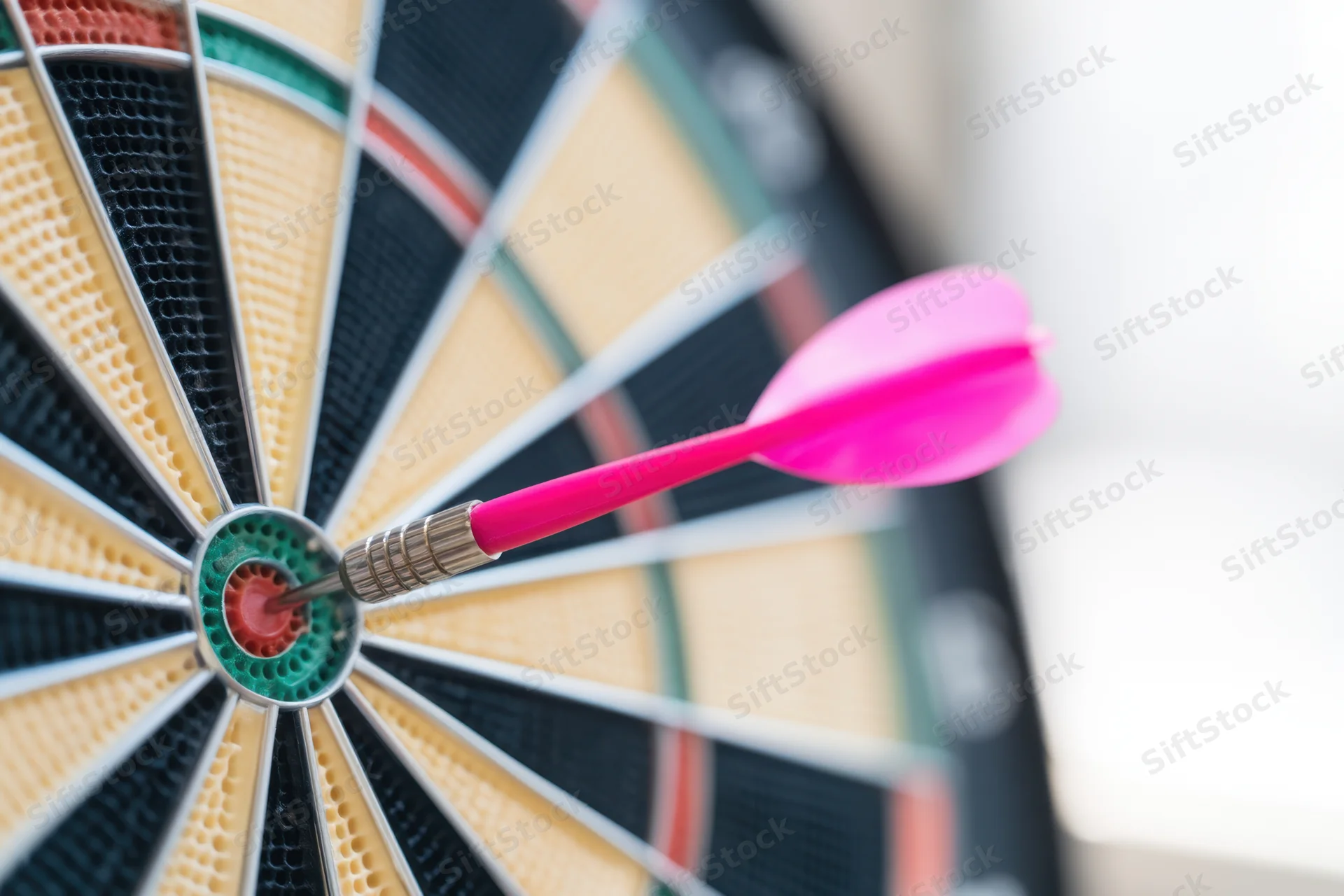 Pink dart hitting the bullseye of a dartboard in close-up view