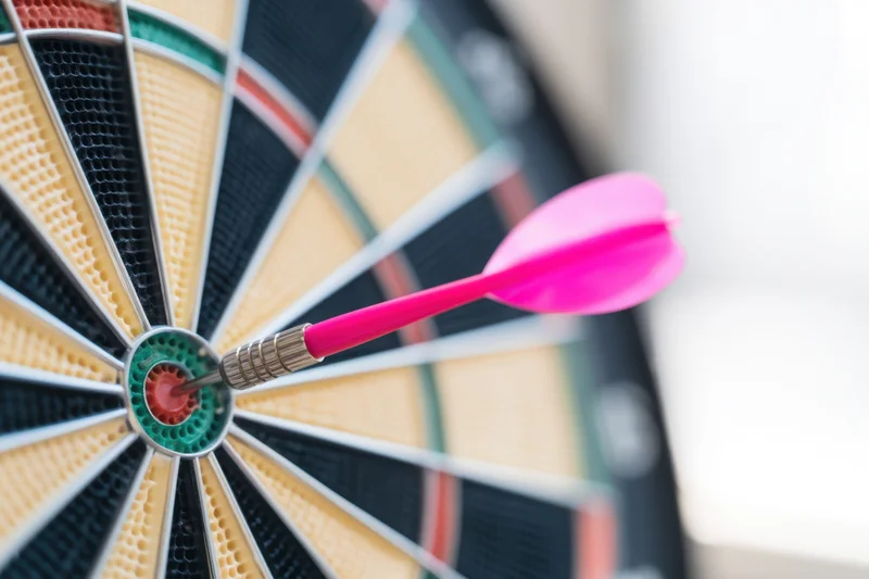 Pink dart hitting the bullseye of a dartboard in close-up view