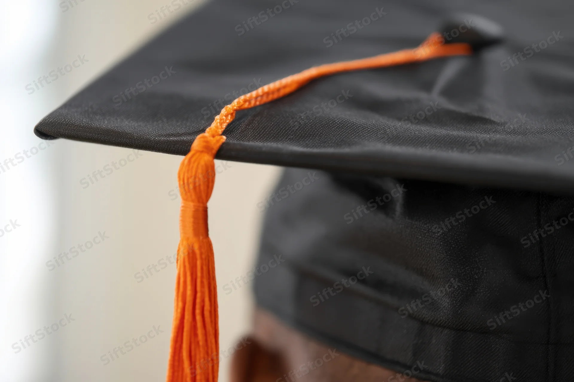 Close-up of a black graduation cap with an orange tassel on a person's head