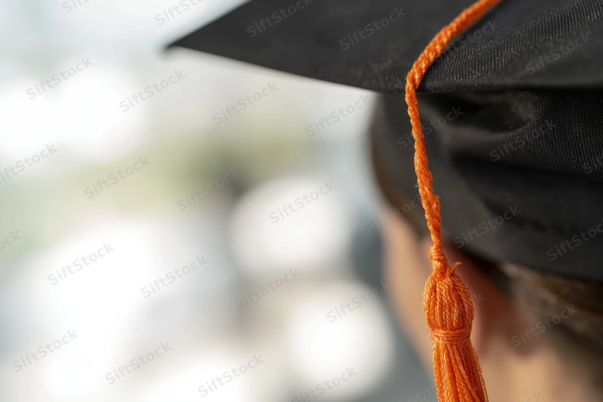 Close-up of a black graduation cap with an orange tassel hanging down