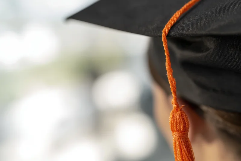 Close-up of a black graduation cap with an orange tassel hanging down
