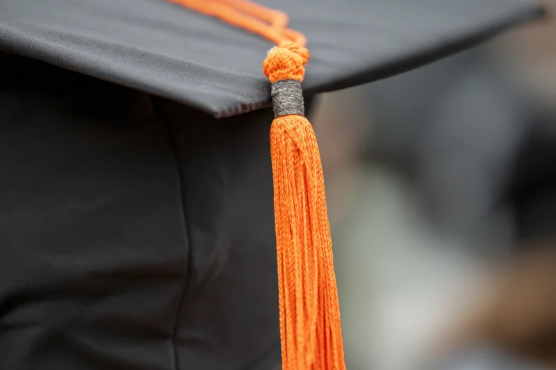 Close-up of a black graduation cap with an orange tassel hanging from the corner