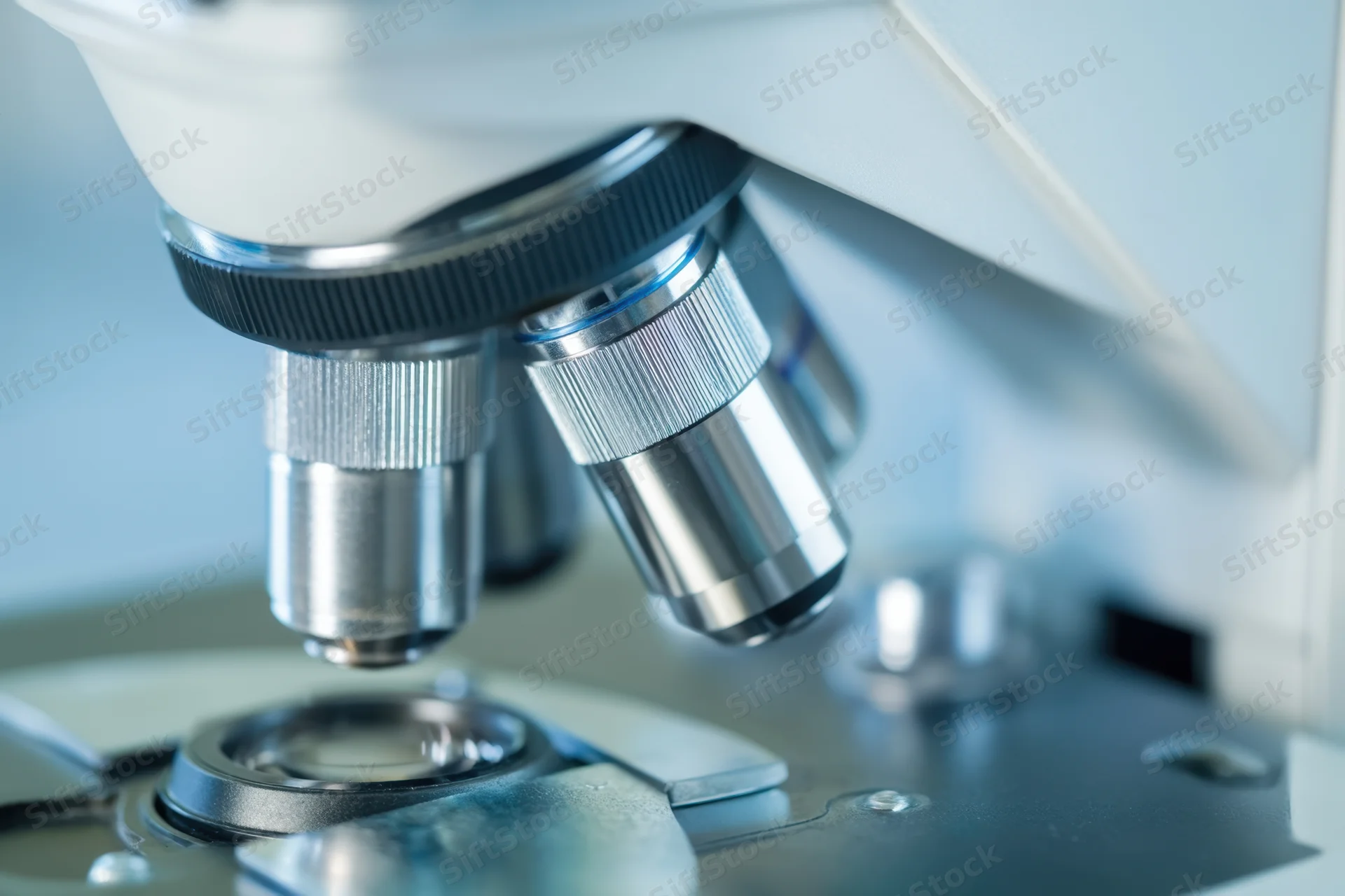 Close-up of microscope objective lenses above a slide stage in a laboratory setting