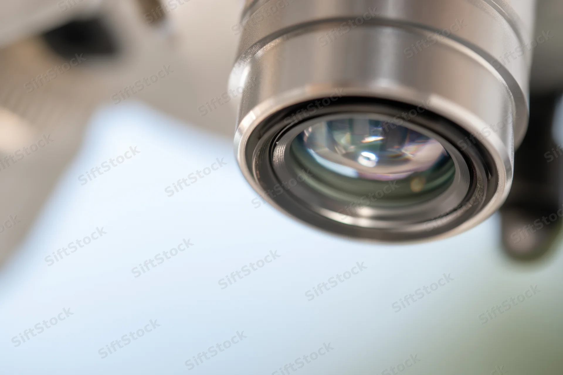 Close-up of a microscope lens showing its glass and metallic housing with reflections, set against a blurred background