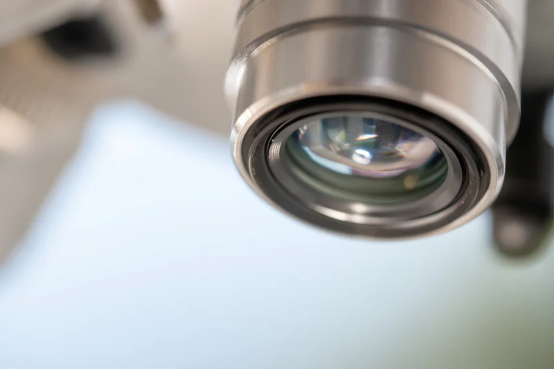 Close-up of a microscope lens showing its glass and metallic housing with reflections, set against a blurred background