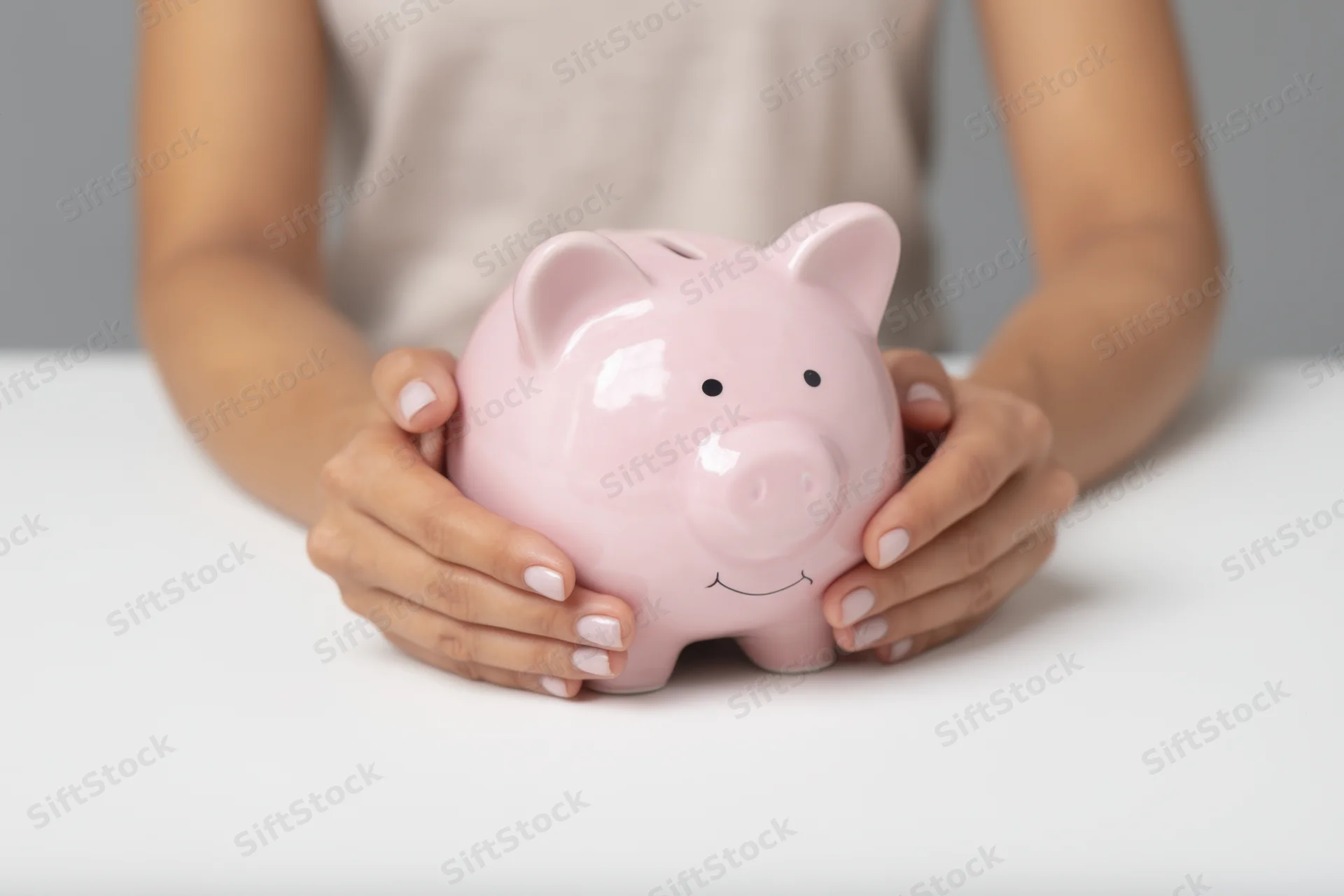 Woman holding pink ceramic piggy bank on white table