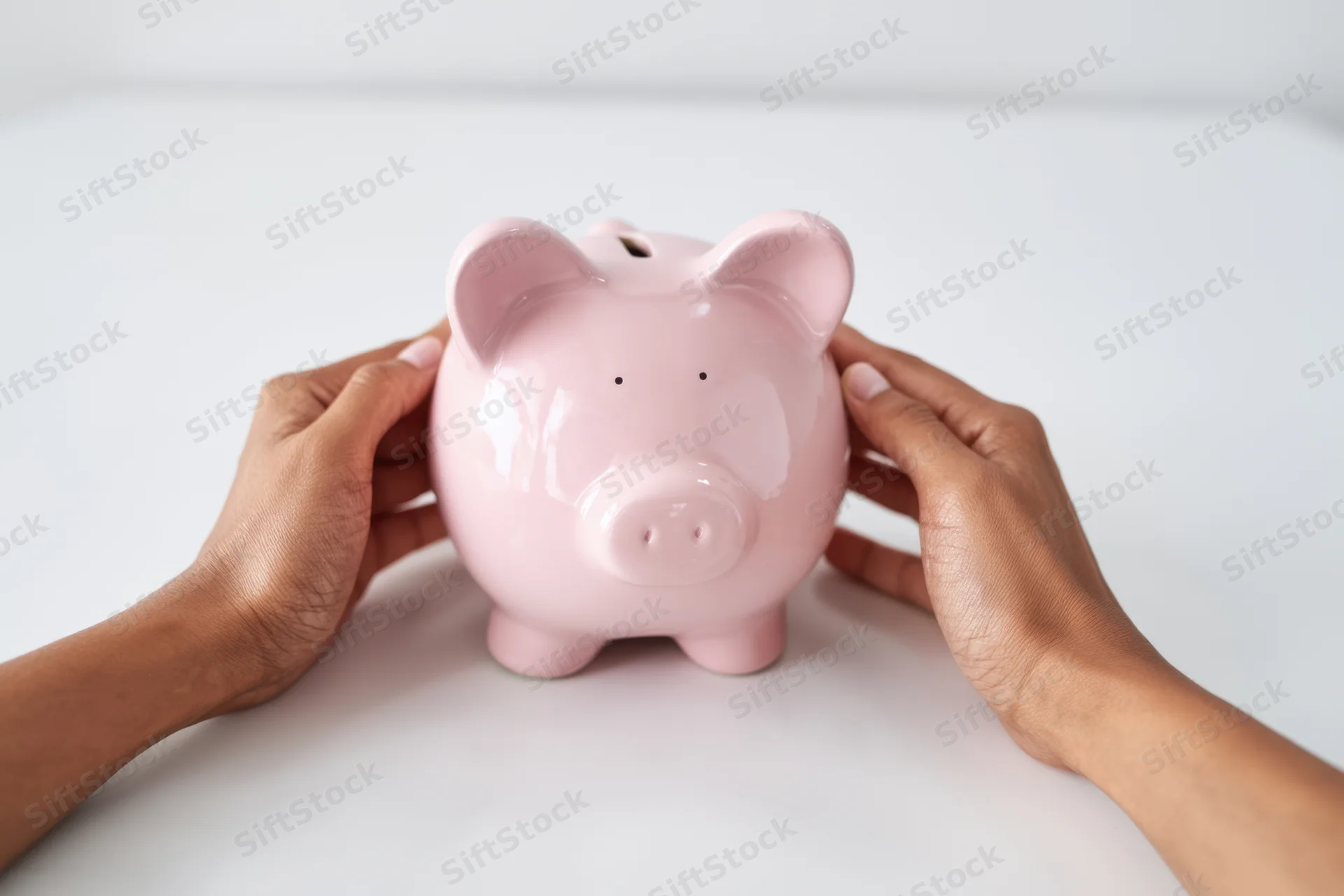 Hands holding a pink ceramic piggy bank on a white tabletop