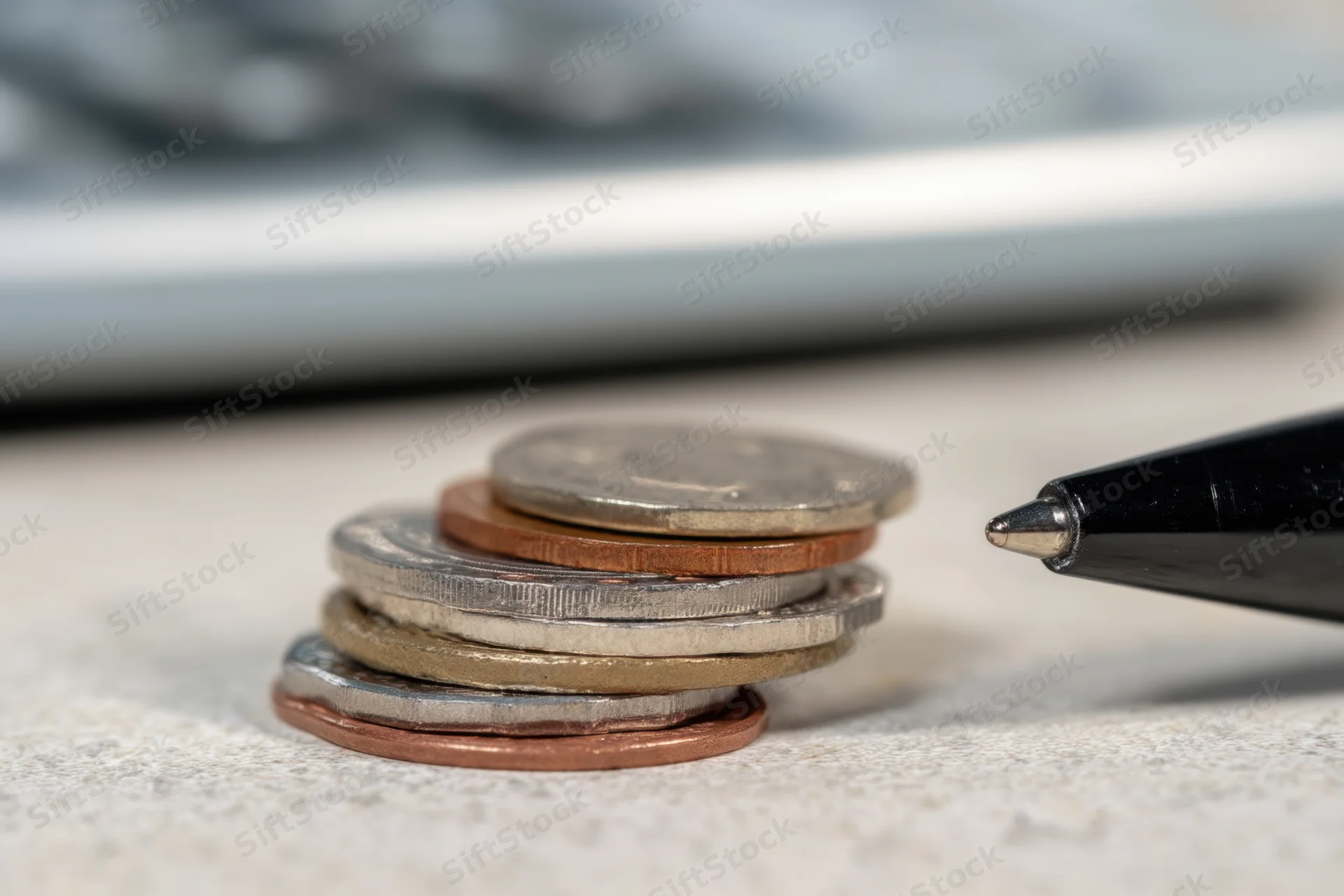 Stack of coins with various denominations on a desk surface next to a pen