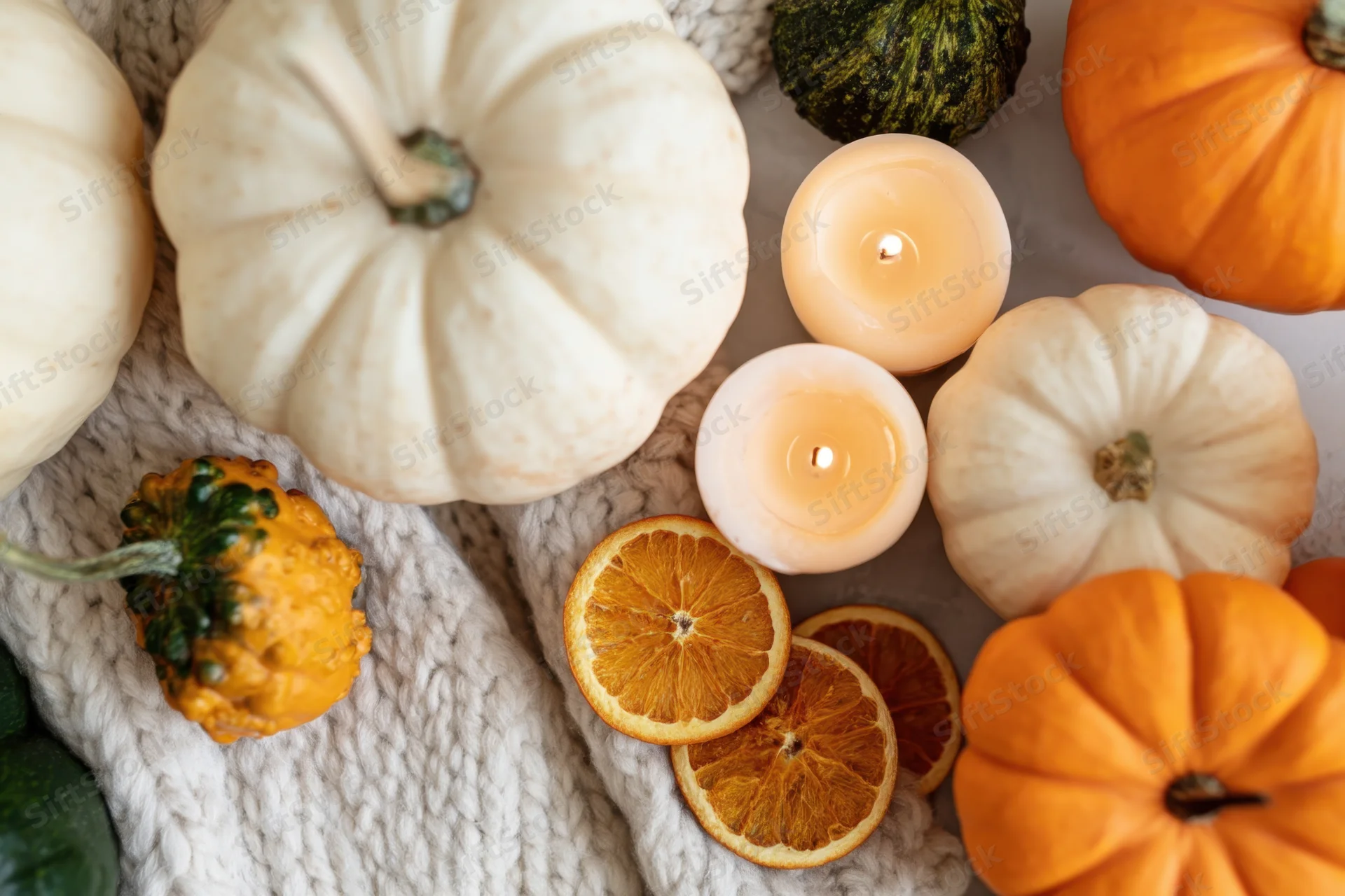 Autumn pumpkins and candles arranged on a knit sweater with dried oranges and gourds
